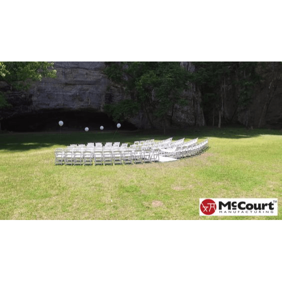 McCourt Gala White Resin Folding Chair With Padding At An Outdoor Event In An Open Lawn Area